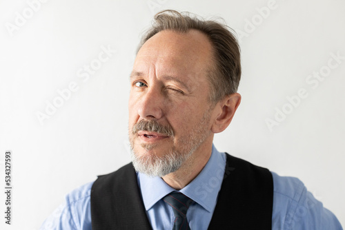 Close-up of mature businessman winking at camera. Senior Caucasian manager wearing formalwear looking at camera and hinting against white background. Flirt or hint concept