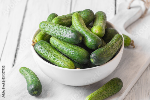 Fresh ripe organic small gherkin cucumbers in bowl on wooden table, not marinated vegetable, cornichon