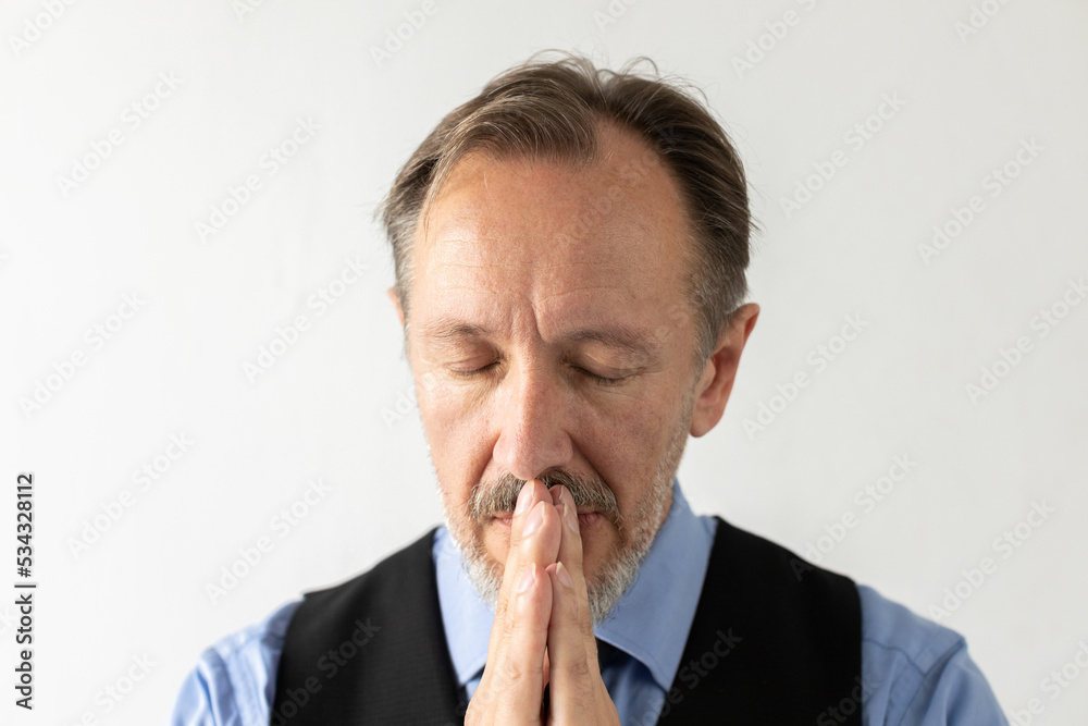 Close-up of mature businessman praying with eyes closed. Portrait of senior Caucasian manager wearing formalwear pleading against white background. Hope and faith concept Close-up of mature businessman praying with eyes closed. Portrait of senior Caucasian manager wearing formalwear pleading against white background. Hope and faith concept