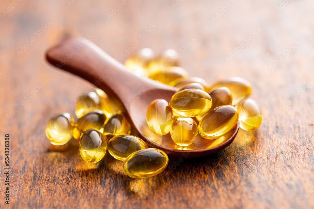 Fish oil capsules in spoon. Yellow omega 3 pills on wooden table. Fish oil capsules in spoon. Yellow omega 3 pills on wooden table.