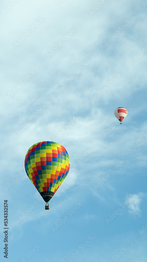 vertical photo two multi-colored balloons fly high in the sky
