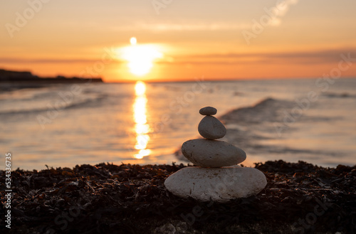Stones stack together by the beach against the sunset. 