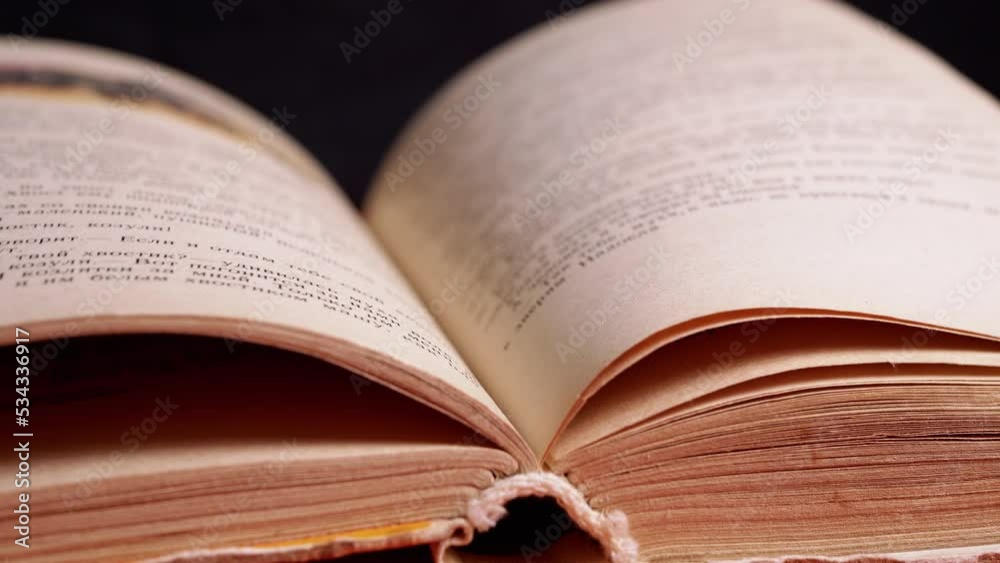 Female Fingers Leafing Through Pages of Old Shabby Book on a Black Background. Reading. Rough papyrus paper on a thick antique book from yesteryear. Orange color. Education. Knowledge. Mystic. Female Fingers Leafing Through Pages of Old Shabby Book on a Black Background. Reading. Rough papyrus paper on a thick antique book from yesteryear. Orange color. Education. Knowledge. Mystic.