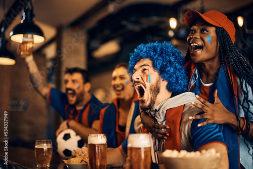 Fotografia Passionate soccer fans scream while watching game on TV in pub.