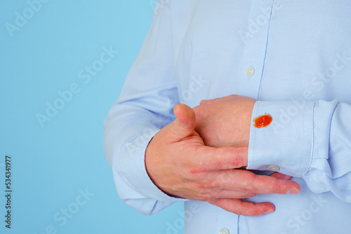 An unrecognizable man showing a stain of sauce on his arm cuff with his hand. isolated on blue background. daily life dirty stain concept