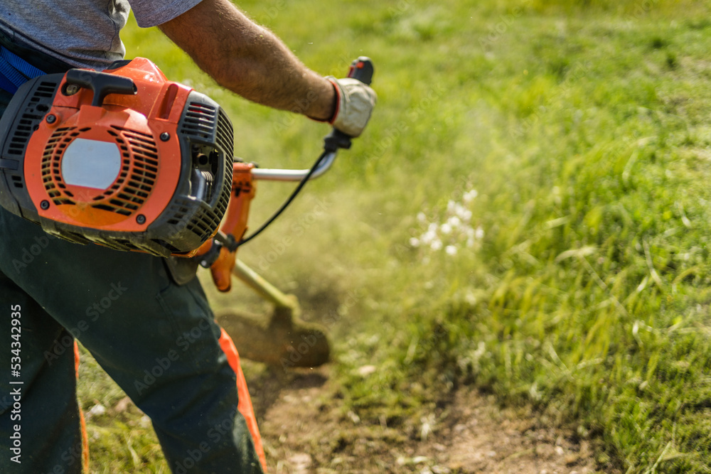 Unrecognizable person trimming grass with a trimmer machine. Unrecognizable person trimming grass with a trimmer machine.