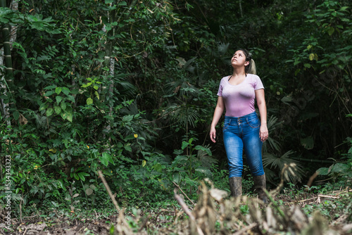 nature-loving woman walks through the jungle looking and exploring while hiking, looking up with curiosity in the middle of a colombian forest. new places. university student exploring.