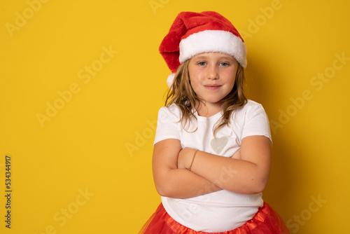 little girl in red santa hat with arms folded on yellow background. portrait © Danko