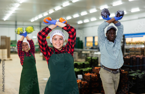 Portrait of smiling male and female workers posing and having fun at warehousing with crop of organic vegetable