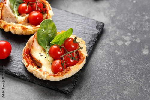 Mini Pizzas with tomatoes, cheese and ham. Small homemade pizza, open pie on slate board and dark background.
