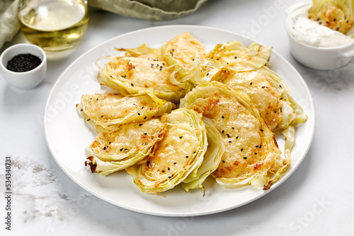 Baked cabbage pieces, roasted cabbage steaks with cheese on white plate and marble background. Vegan diet, healthy food.