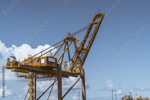 Close-up view of a heavy huge harbor crane in front of a beautiful skyscape, with a big cabin, many stairways, cables, and passages with fences on its top; a copy space area on the right