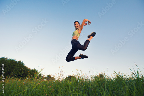Young woman jumping and exercise in the nature on a sunny summer day