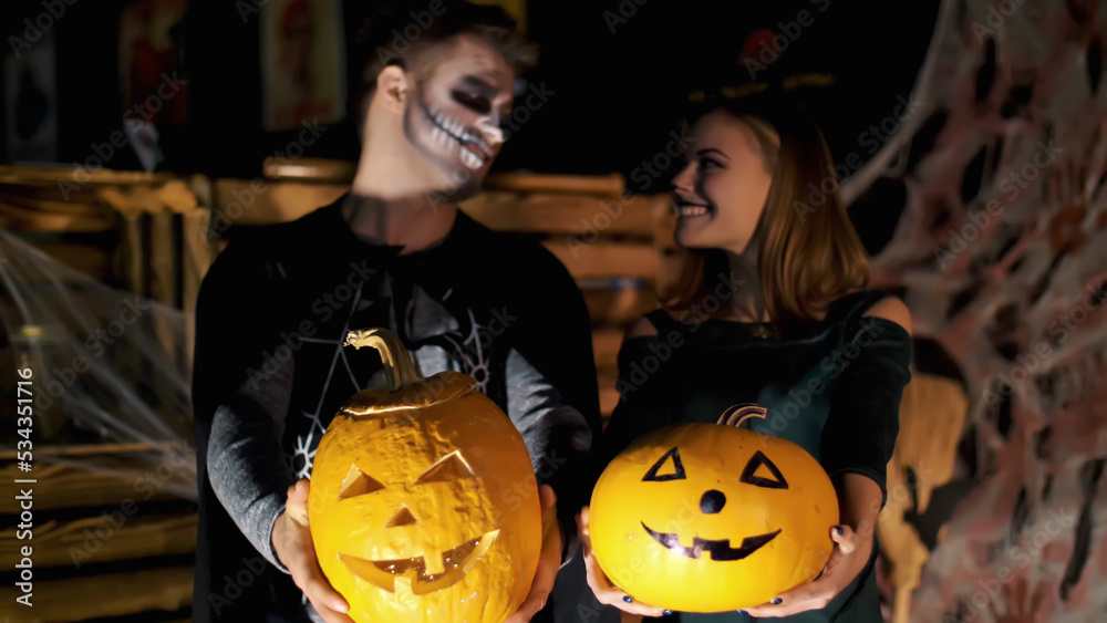 date in style of Halloween party, night, twilight, in the rays of light, guy with a girl dressed in costumes and with a terrible makeup are holding two large Halloween pumpkins. High quality photo date in style of Halloween party, night, twilight, in the rays of light, guy with a girl dressed in costumes and with a terrible makeup are holding two large Halloween pumpkins. High quality photo