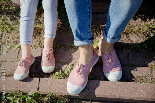 legs of mom and daughter sitting on the steps in pink sneakers and jeans