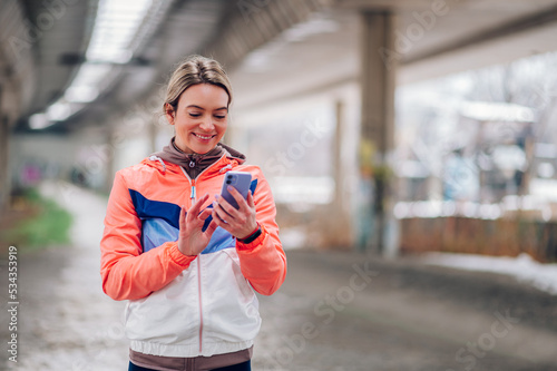 Young woman taking a break from jogging outside and using smartphone