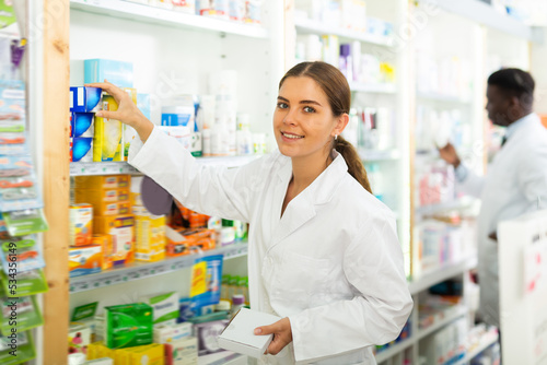 Portrait of a young female pharmacist laying out goods on the shelves of a rack in a pharmacy