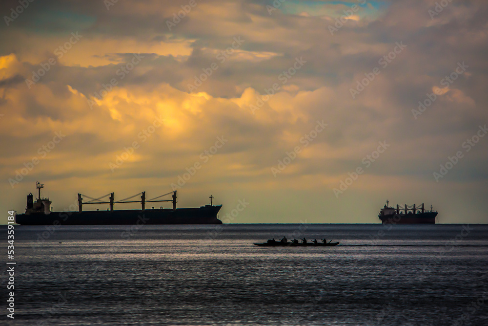 Container ship and Indian canoe in Vancouver harbor, Canada, with dramatic sky