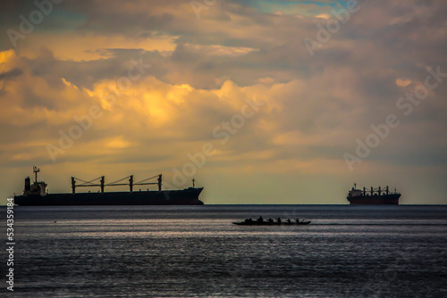Container ship and Indian canoe in Vancouver harbor, Canada, with dramatic sky