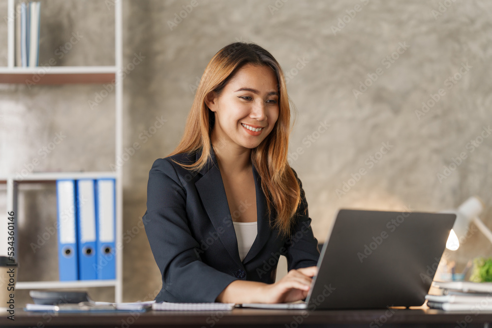 Using laptop, Young pretty asian stock manager checking list of product and working at workstation.