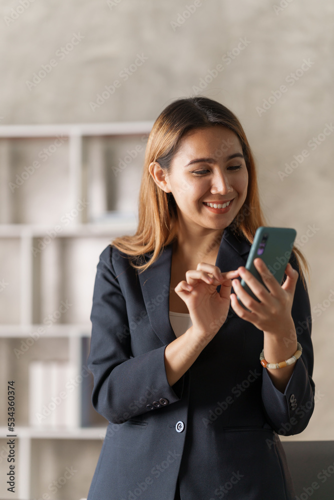 Young pretty asian stock manager checking list of product and working at workstation, using mobile phone. Young pretty asian stock manager checking list of product and working at workstation, using mobile phone.