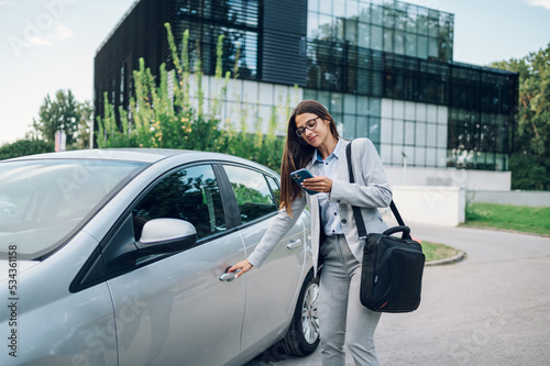 Business woman getting into the car and using smartphone