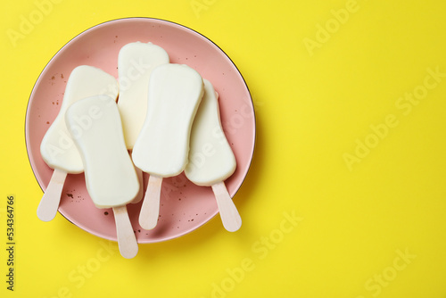 Plate with glazed ice cream bars on yellow background, top view. Space for text