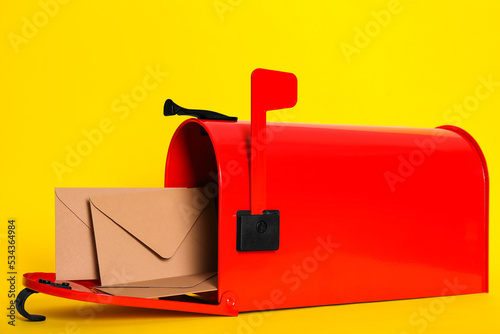 Open red letter box with envelopes on yellow background, closeup