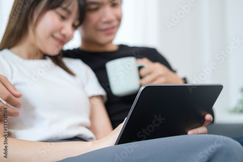 Affectionate young couple watching movie or shopping online in internet store on digital tablet, relaxing on couch at home.