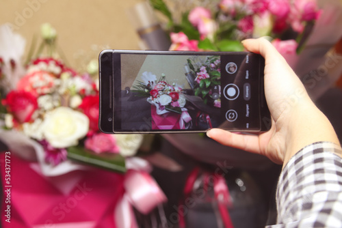 Defocus male hand taking photo of colorful roses with cell, mobile phone. Woman with a gift of flowers. Female florist with many roses bunches and bouquets. Florist. Out of focus