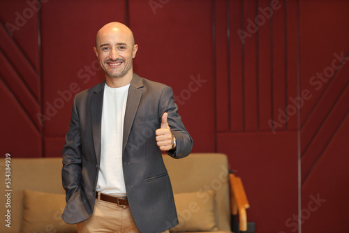 Portrait of attractive and handsome caucasian businessman in suit standing and showing thumb up while look at camera with confident happy face in modern office. Success business and technology concept