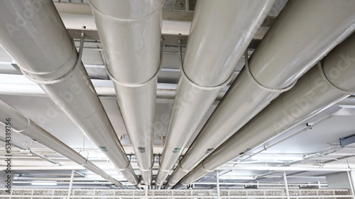 Sanitary pipes under the building. Closeup of white metal plumbing pipes installed under the ceiling or inside the building and maintenance of drains. Selective focus