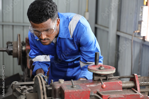 Technician mechanic or worker man in protective uniform using metal lathe machine operate polishing car disc brake at garage. Maintenance automotive and inspecting vehicle part concept