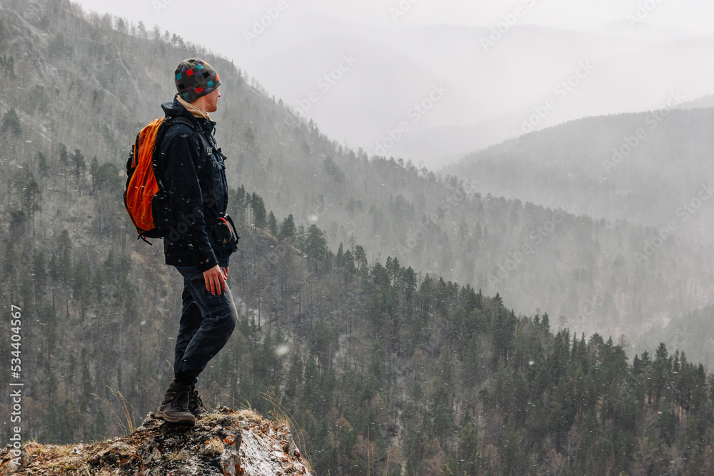 A male hiker enjoys a beautiful view of the mountains in a snowfall. A male hiker enjoys a beautiful view of the mountains in a snowfall.