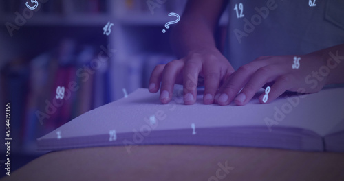 Digital composition of numbers and symbols floating against mid section of boy reading a book in bra