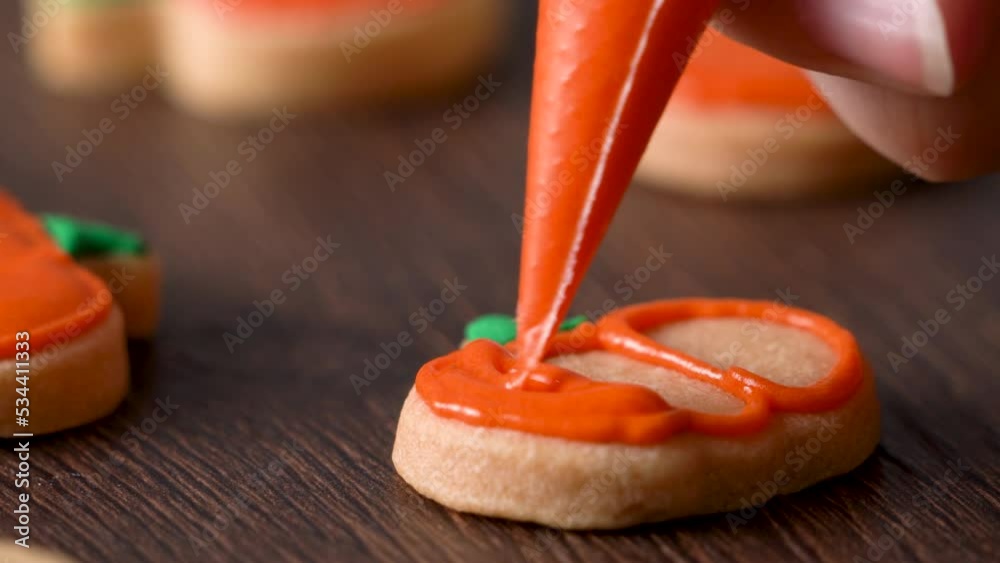 Decorating cute Halloween pumpkin cookies with frosting in icing bag.