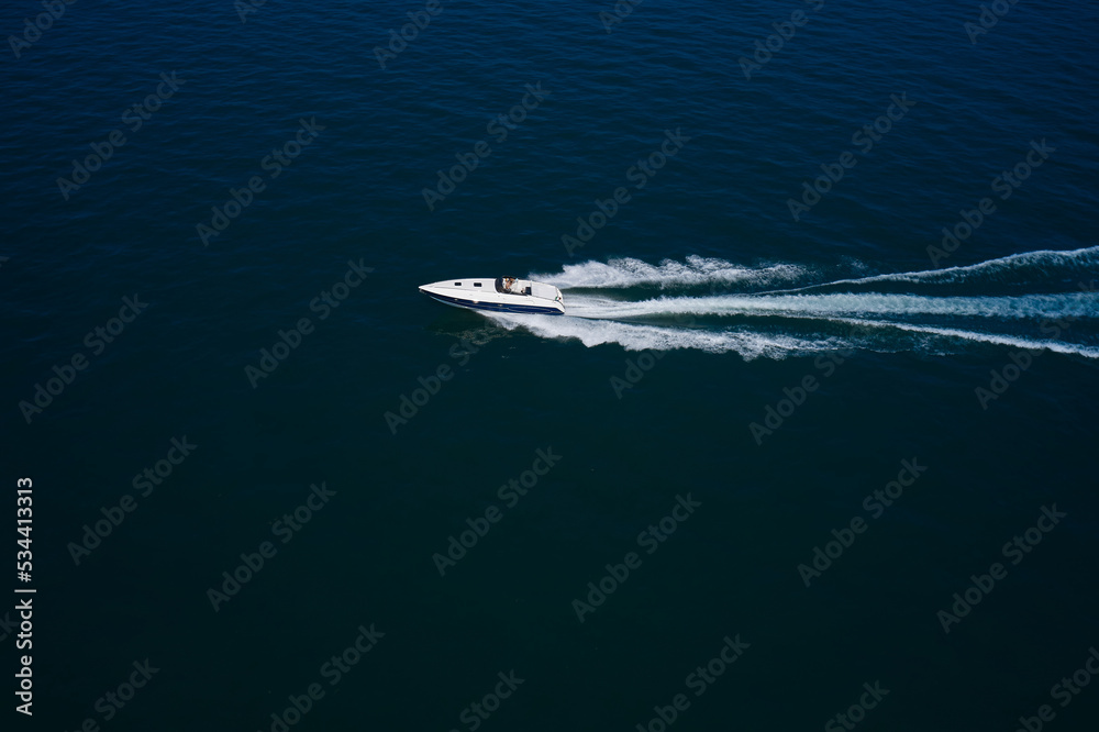 Luxurious Blue boat motorboat rushes through the waves of the blue Sea. Boat fast moving aerial view. Luxurious boat fast movement on dark water. Luxurious Blue boat motorboat rushes through the waves of the blue Sea. Boat fast moving aerial view. Luxurious boat fast movement on dark water.
