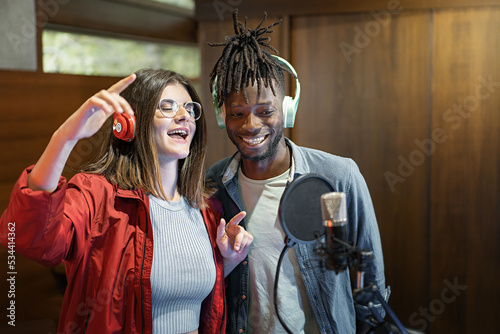Excited multiethnic couple with microphone and headphones of young broadcasters singing music live and having fun online - Social network content creators duet - people, technology lifestyle concept
