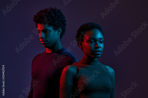 Young man and woman in neon light over dark background