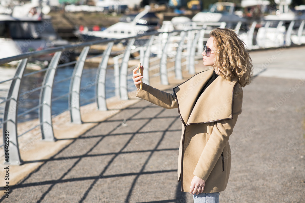 A young girl takes a selfie on a mobile phone camera in the city on an autumn sunny day. A young girl takes a selfie on a mobile phone camera in the city on an autumn sunny day.