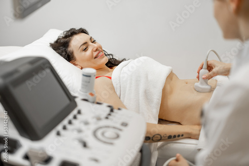 Happy adult woman during an ultrasound examination of the abdominal cavity at modern medical office. Concept of women's health and examination during pregnancy