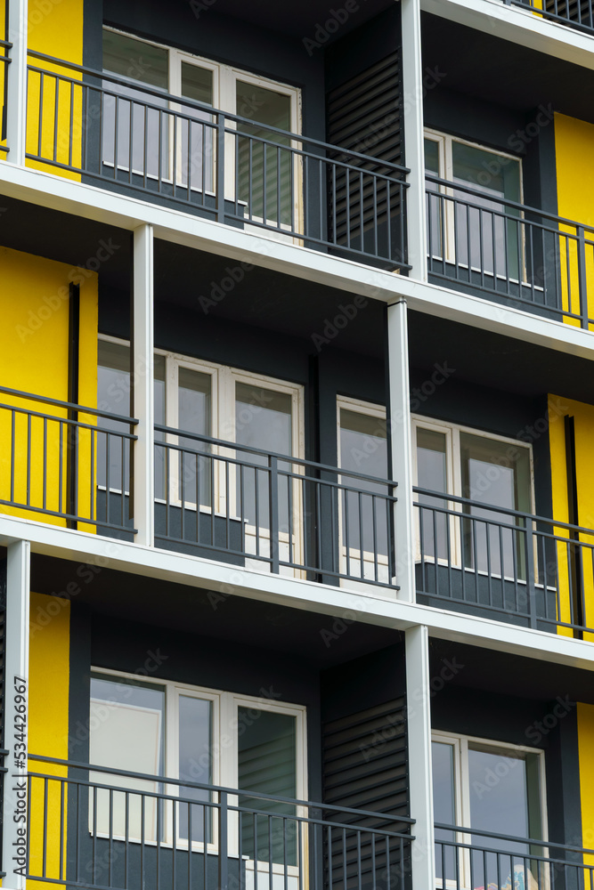 the facade of a modern multi-storey building, windows and balconies, yellow and black walls, the concept of urbanism and city construction