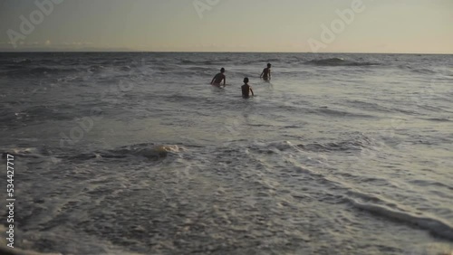 A wide shot of dramatic sea golden hours and kids swimming, Lombok, West Nusa Tenggara