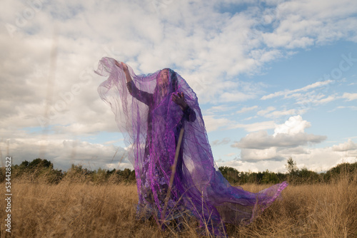 Fine art portrait of woman in the field dancing in long dress under purple veil photo