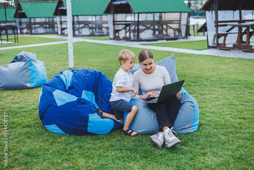 Little boy having fun sitting on sack in summer or spring in park outdoors. Family vacation of mother and son in the fresh air