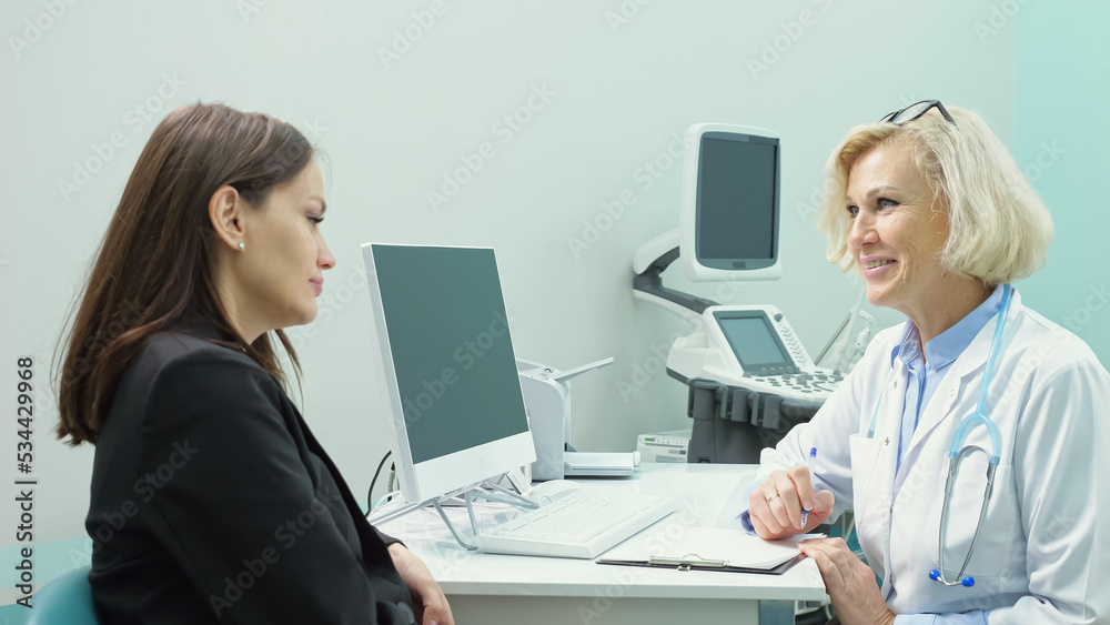 Mature blonde doctor writes down complaints in patient checklist form. Young woman describes complications to respiratory system after taking heavy antibiotics Mature blonde doctor writes down complaints in patient checklist form. Young woman describes complications to respiratory system after taking heavy antibiotics