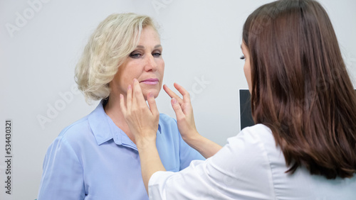 Experienced doctor gives cosmetological consultations to mature woman in beauty clinic. Brunette beautician plans face and neck lifting for joyful patient, closeup