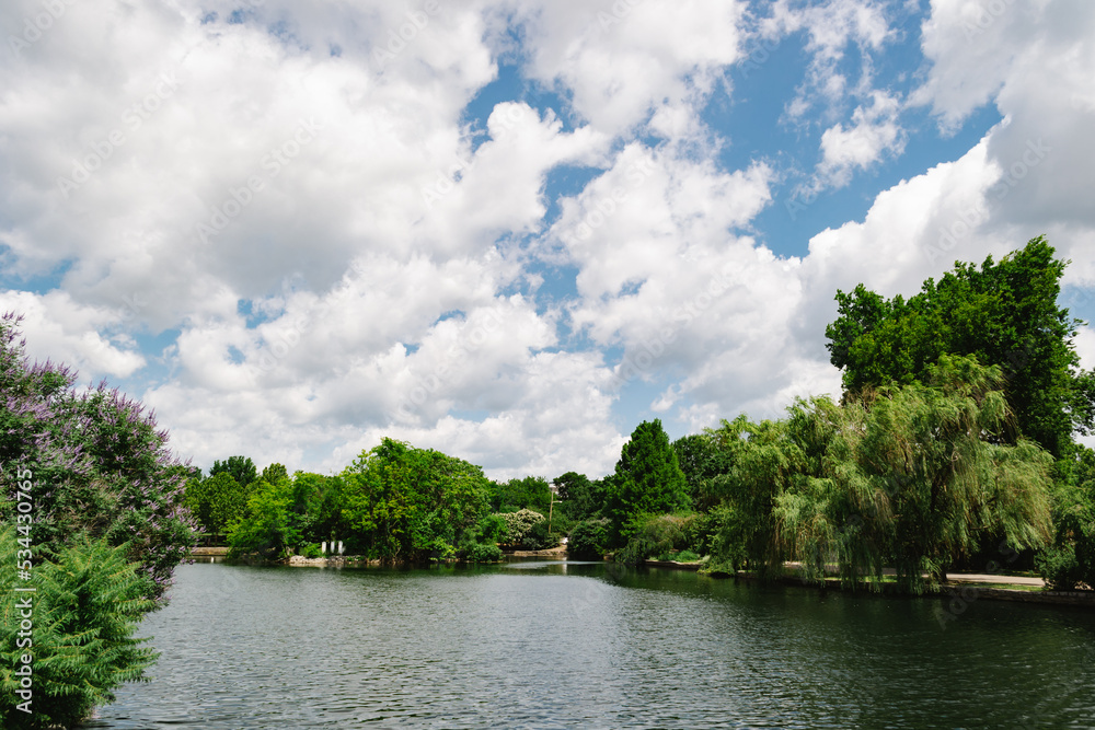 Picture of a river pond surrounded by lush green trees under a cloudy blue sky in the afternoon