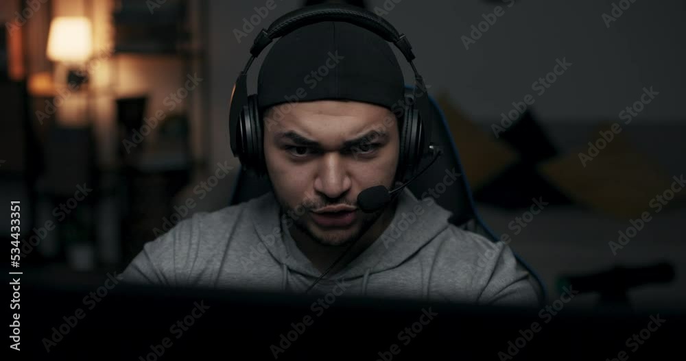 Close-up of bearded guy in cap wearing headphones. Man plays online game, he is finalist and one step away from winning. Guy communicates with opponent. Man is infinitely happy about victory. Close-up of bearded guy in cap wearing headphones. Man plays online game, he is finalist and one step away from winning. Guy communicates with opponent. Man is infinitely happy about victory.