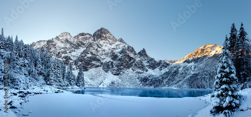 Fototapeta Naklejka Na Ścianę i Meble -  Winter landscape of sunrise in Tatra Mountains. Snow covered fir trees on mountains and lake frozen. Beautiful view on lake and mountains. 
